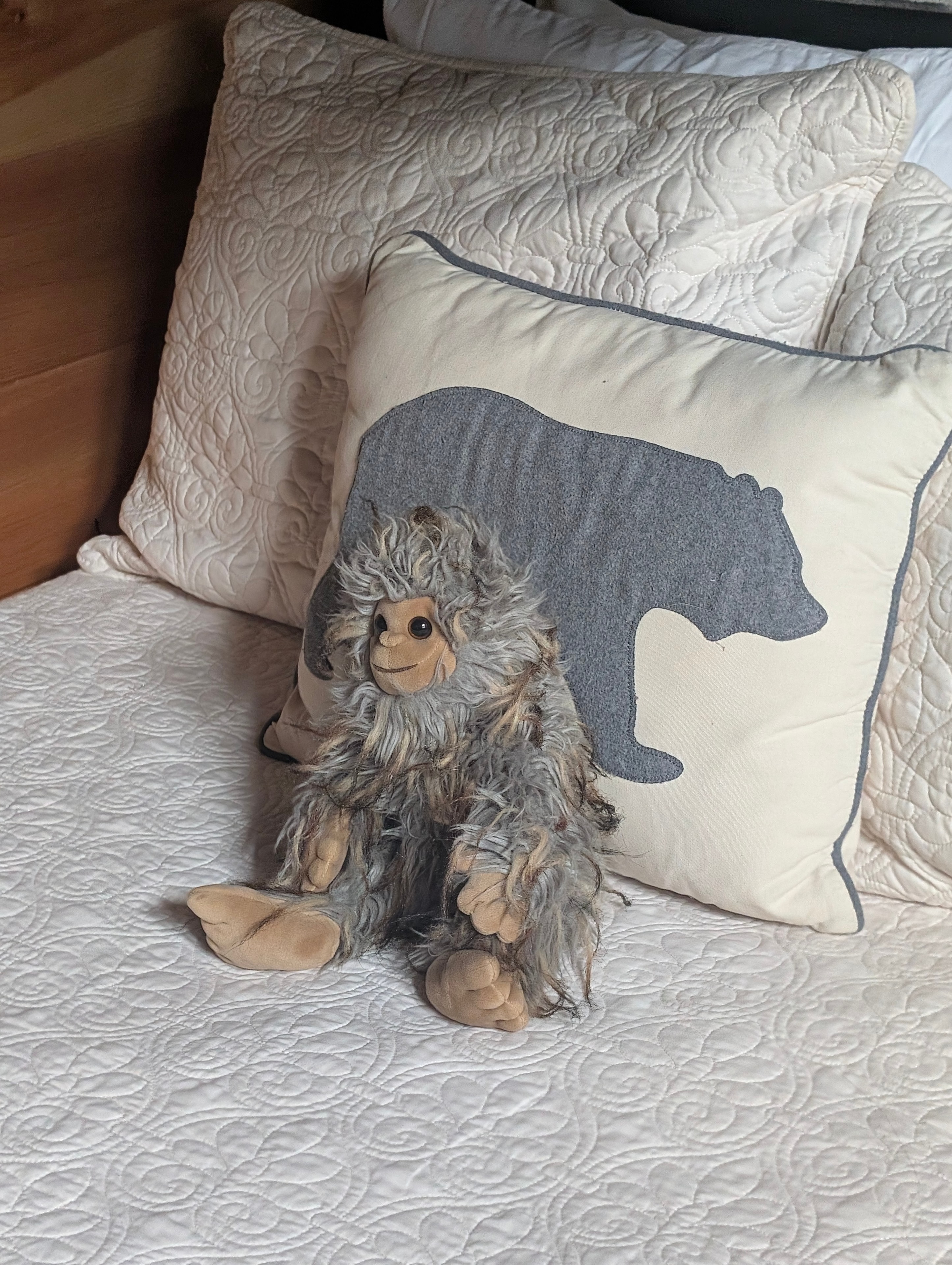 Sasquatch plush toy on bed with bear pillow
